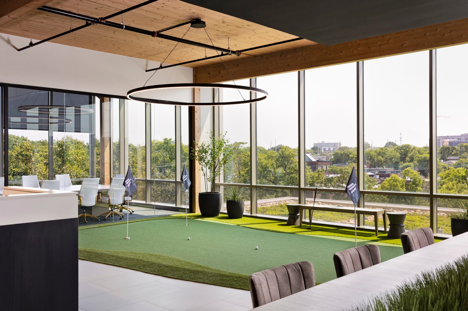 A ring pendant light hangs over an office putting green